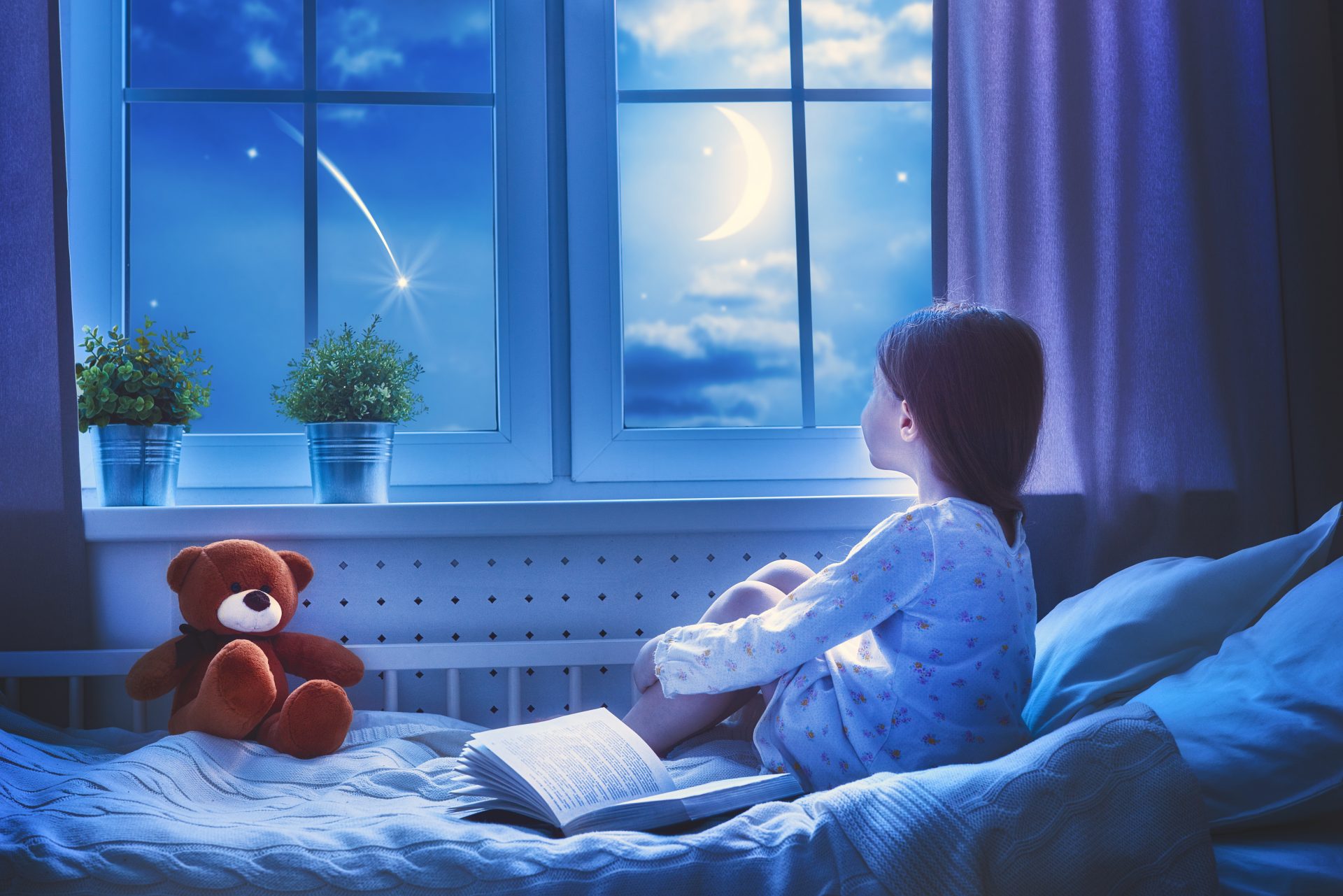 Girl looking out of bedroom window at night needing a blackout blind for better sleep