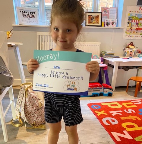 3 year old girl holding up her happy little dreamers sleep certificate because she can sleep through the night now
